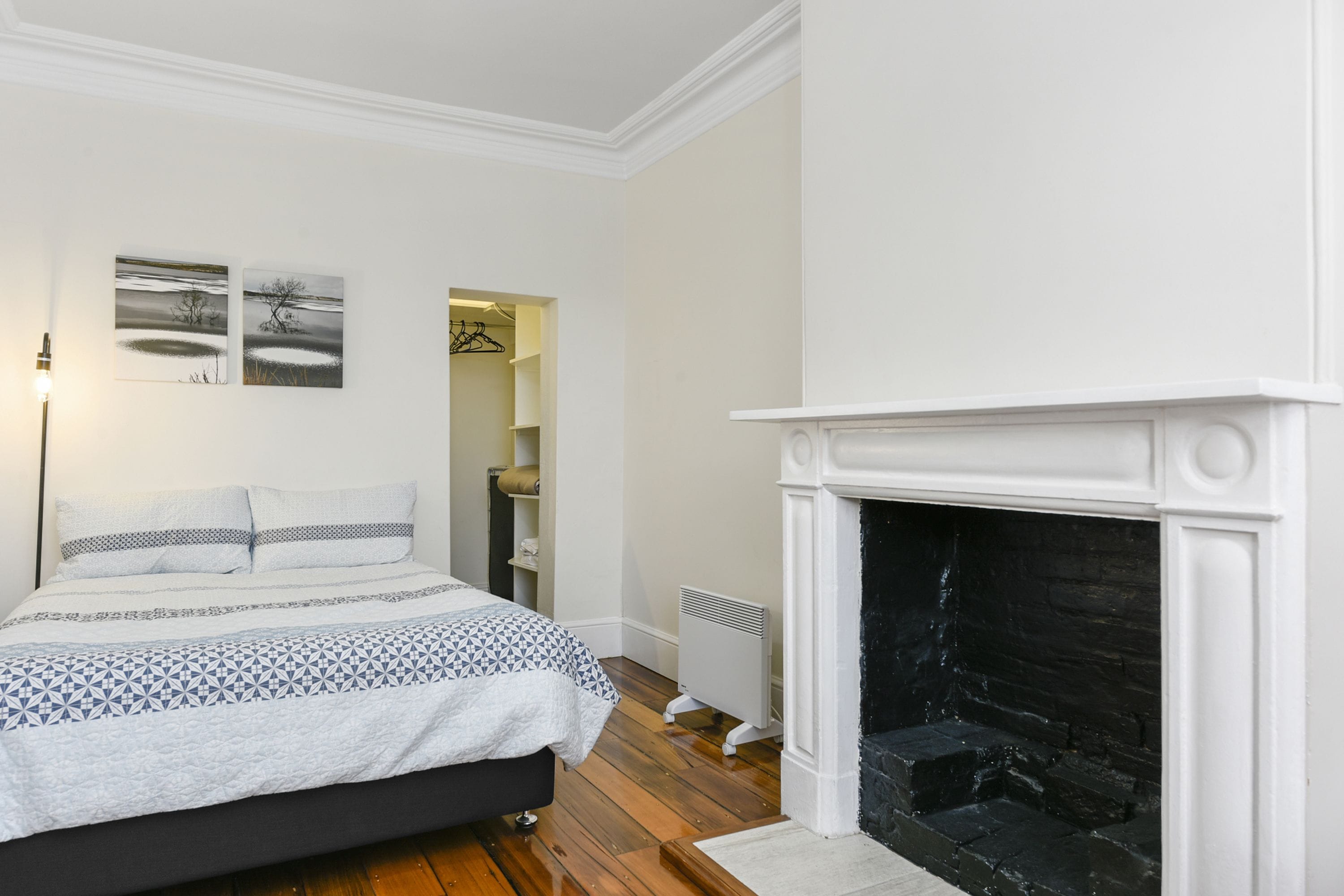 A bedroom with a bed, a fireplace, and two wall-mounted paintings.
