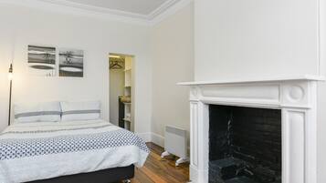 A bedroom with a bed, a fireplace, and two wall-mounted paintings.