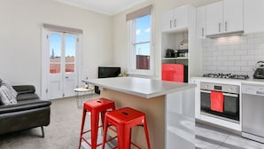 A modern kitchen with white cabinets, a central island, red bar stools, a gas stove, and a red refrigerator. - Trinity Hill Apartments (Hobart)