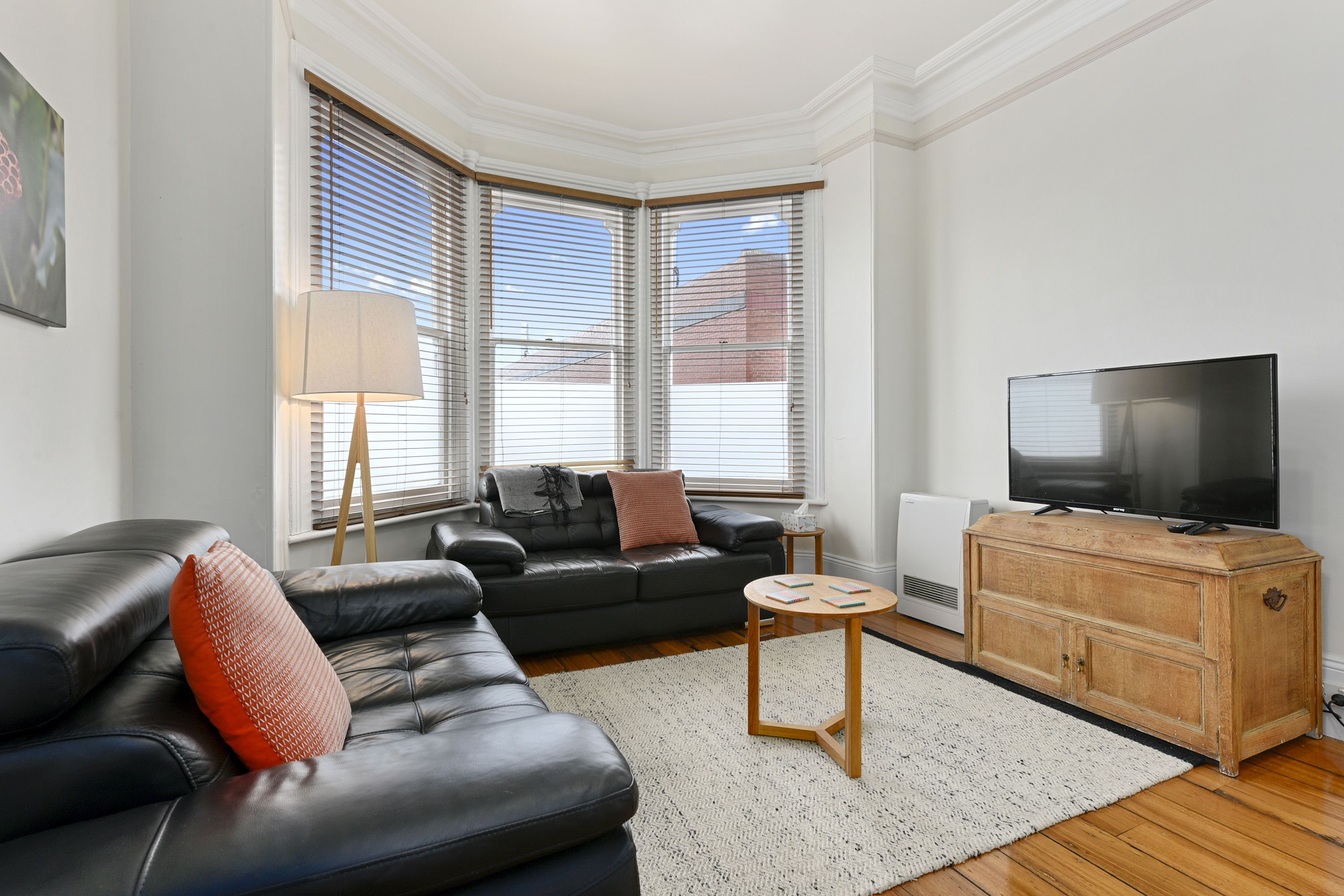 A living room with a black leather sofa, a wooden cabinet, a flat-screen TV, and a lamp.