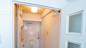 A narrow hallway with a door at the end, a light fixture on the ceiling, and a wall-mounted security device. - Fukuoka Haneul inn (Fukuoka)