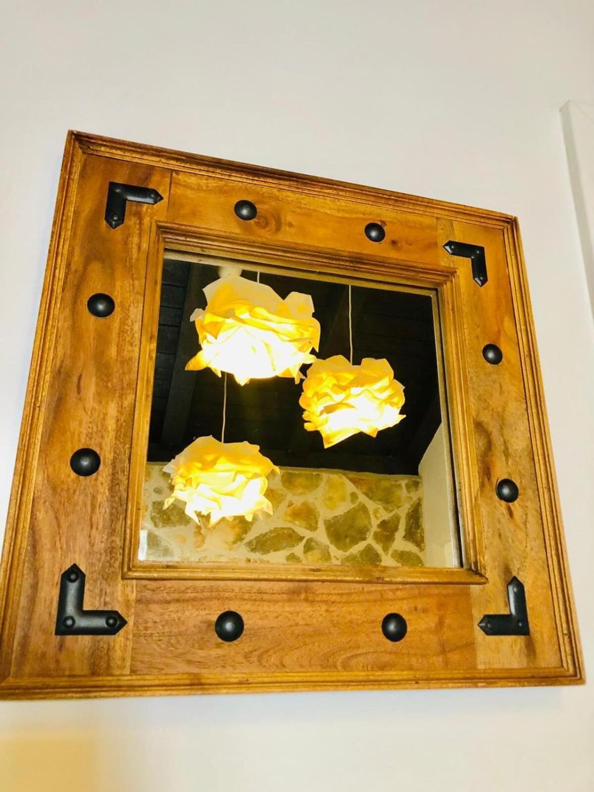A mirror with a wooden frame and black knobs, reflecting three yellow lights.