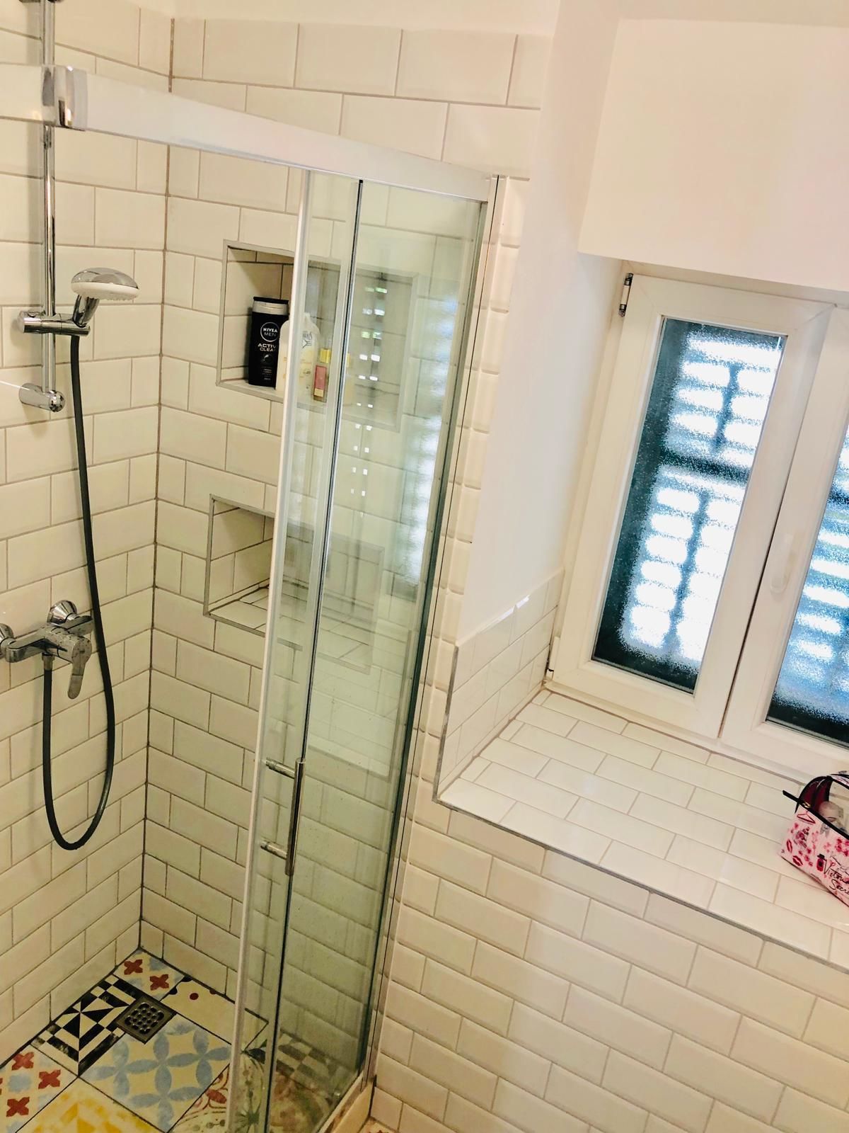 Un espace douche doté d’une porte en verre, d’un pommeau de douche à main et d’un sol carrelé orné d’un motif géométrique.