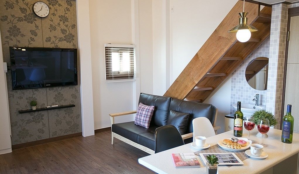 Uma sala de estar moderna com um sofá de couro preto, uma escada de madeira, uma TV fixada na parede e uma área de jantar com uma mesa posta para dois.