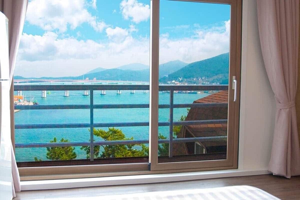 A room with a large sliding glass door leading to a balcony with a view of a bridge over water and mountains.