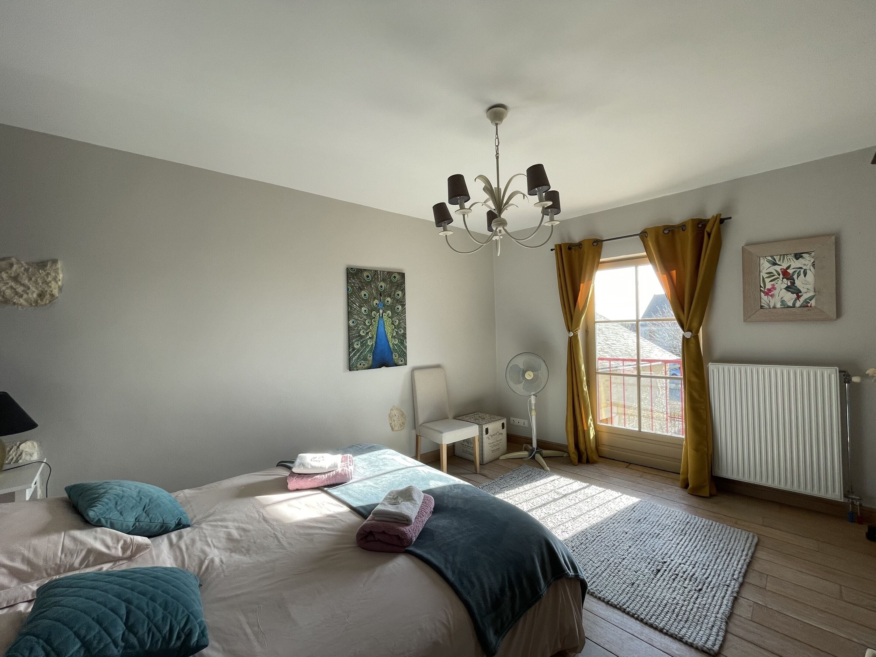 Quarto com cama, ventoinha, radiador e janela com cortinas.