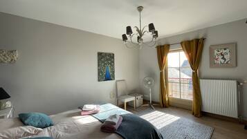 Quarto com cama, ventoinha, radiador e janela com cortinas.
