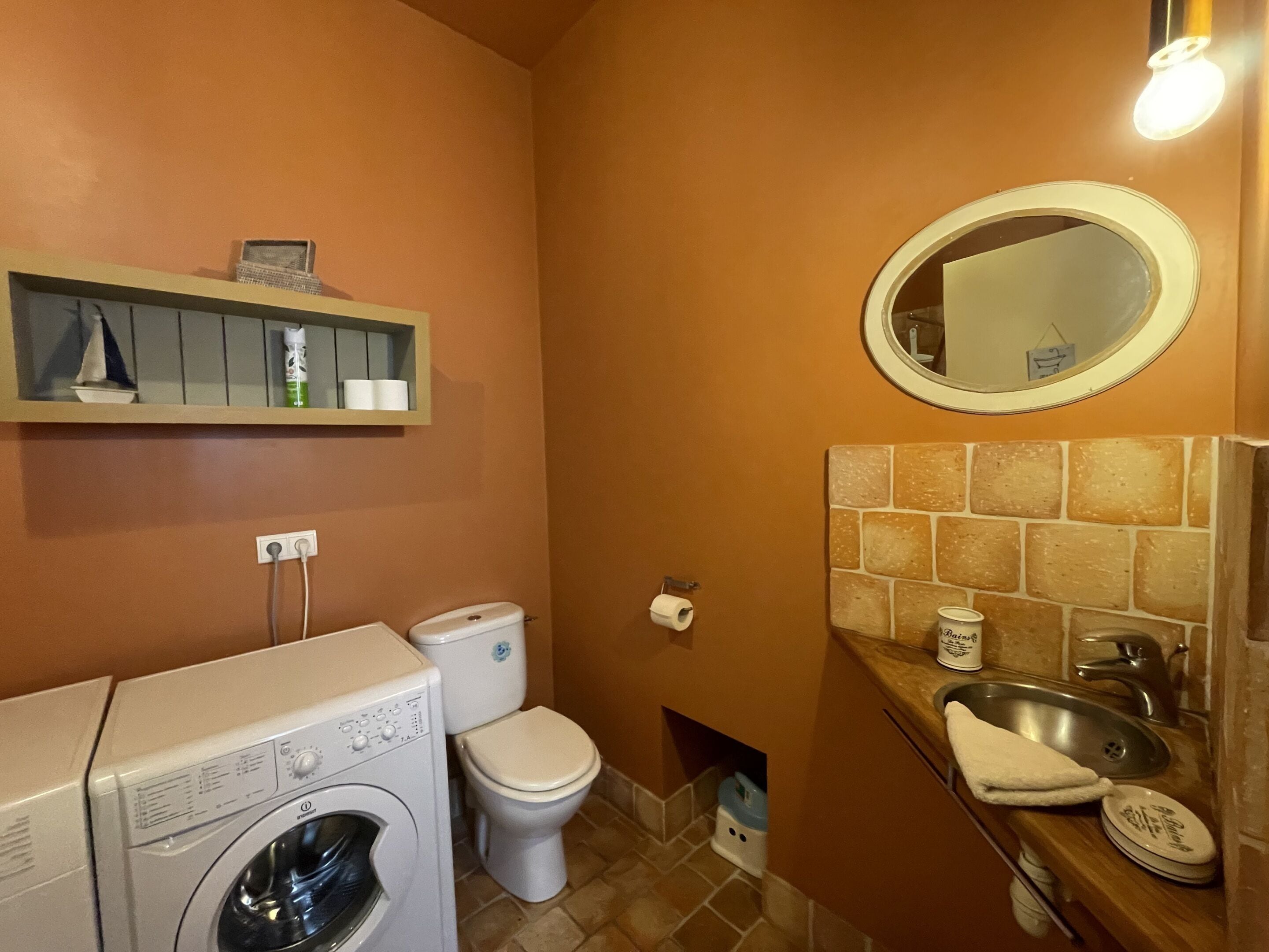 Baño pequeño con lavadora, inodoro y lavamanos con espejo.
