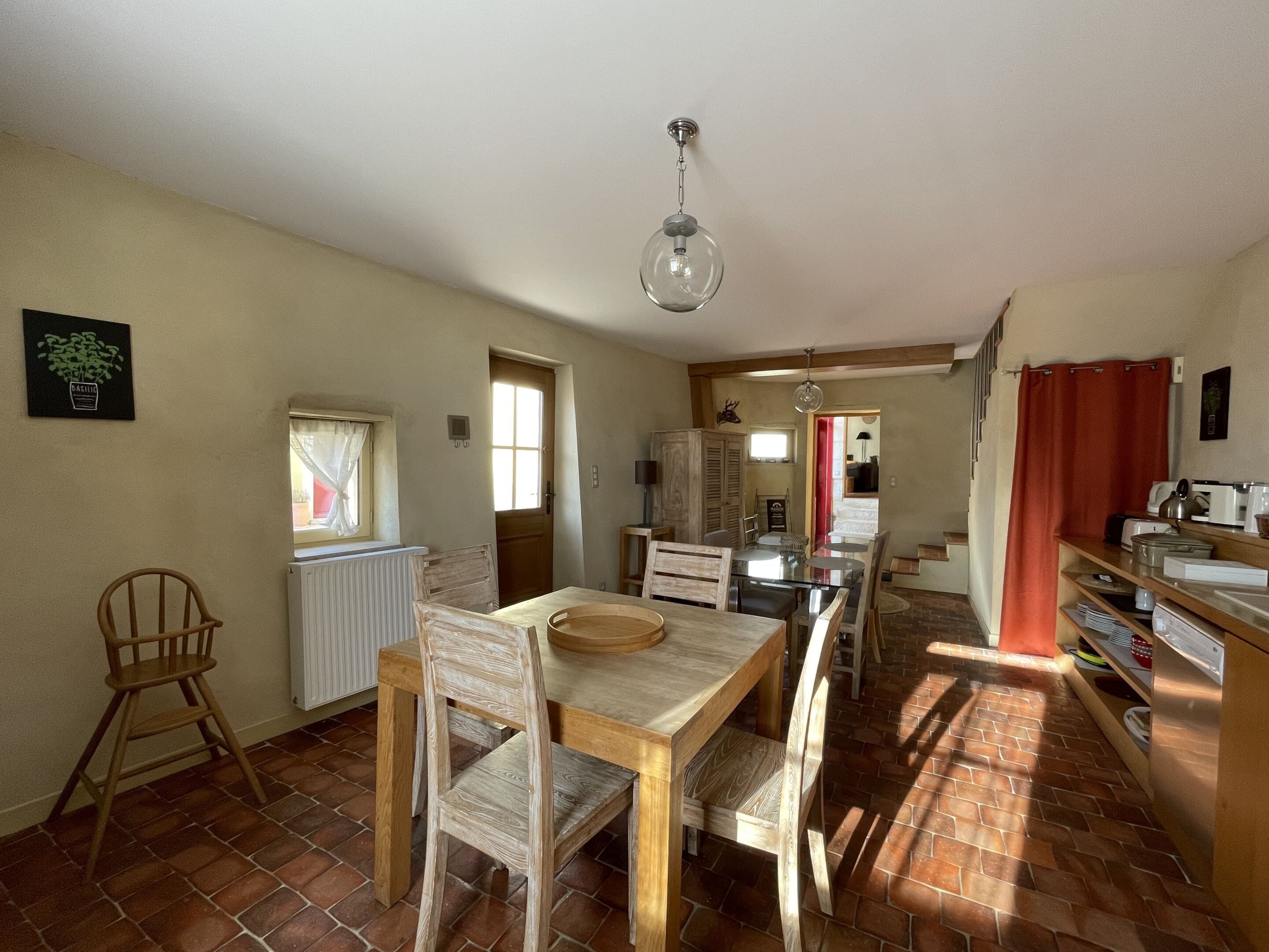 A spacious kitchen with a dining area, a radiator, and a window with curtains.