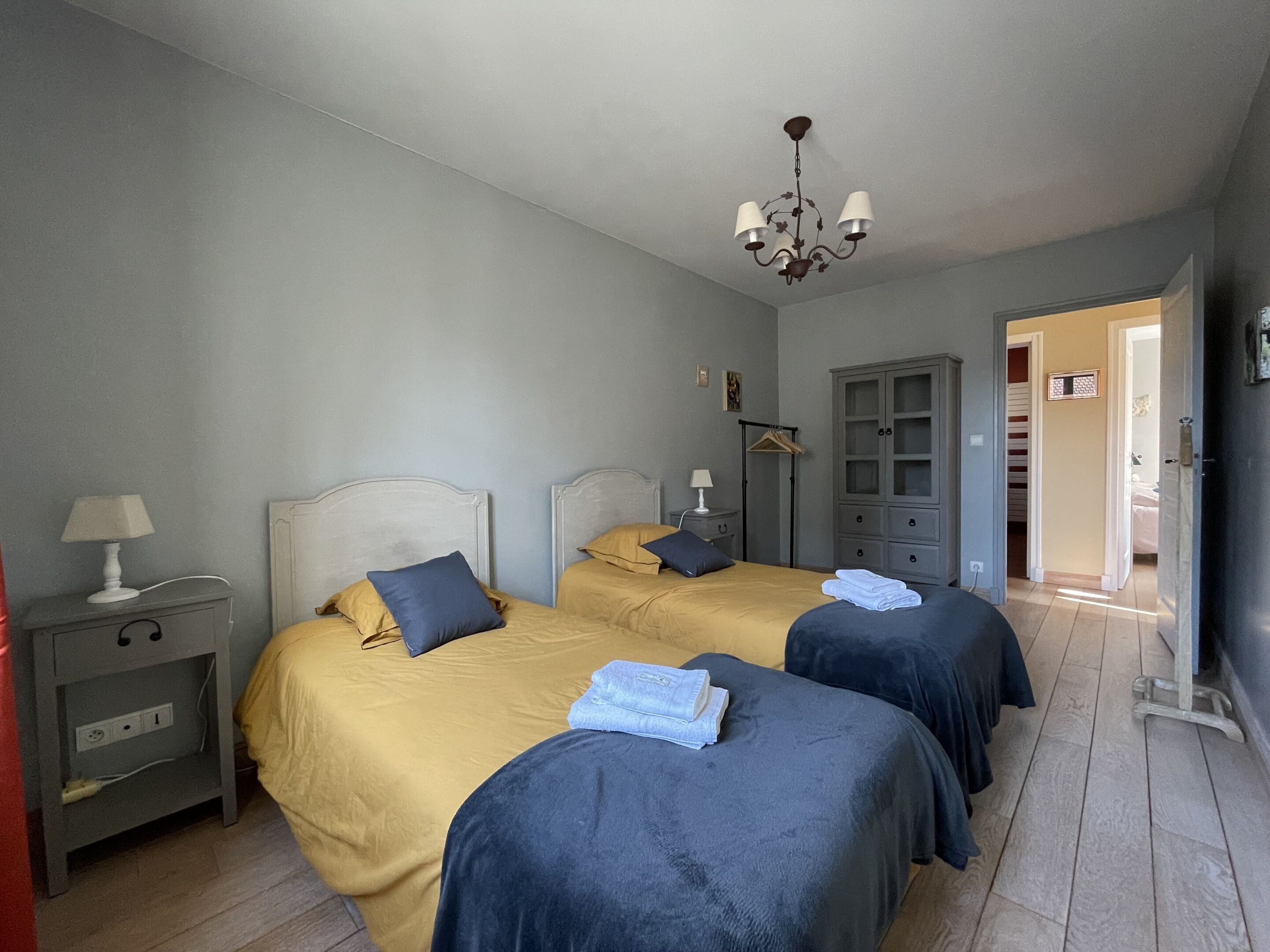 A hotel room with two beds, a wardrobe, a bedside table, and a hanging light fixture.
