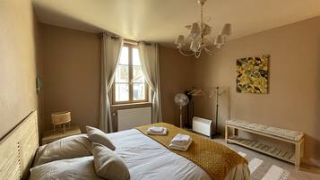 Hotelkamer met een bed, nachtkastje, lamp, radiator, ventilator, een bankje en een raam met gordijnen.