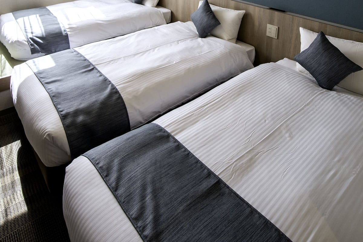Habitación de hotel con dos camas, un ventanal con cortinas y una pared azul de acento.