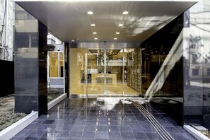 Una entrada de hotel moderna con puerta de cristal, suelo de baldosas e iluminación empotrada en el techo.