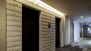 A hallway with a textured wall, a carpeted floor, and a door with a light switch. - Hotel Lantana Naha matsuyama (Naha)