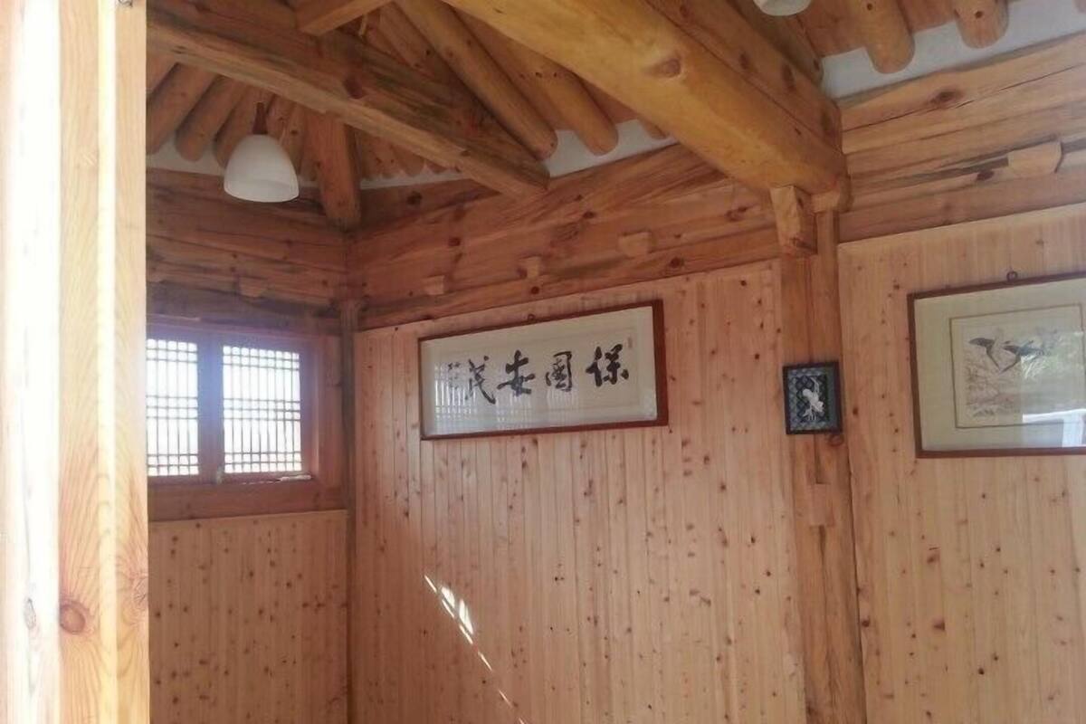 A wooden room with a ceiling beam structure, a framed sign with Japanese characters, and a window with bars.