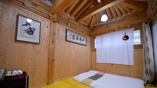 A wooden room with a bed, a framed picture, and a sign on the wall. - Jeonju Geune (Jeonju)