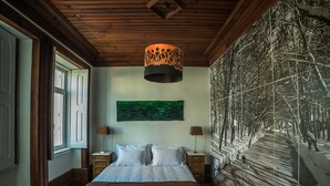 A bedroom with a large bed, two bedside tables, a hanging lamp, and a wall with a nature-themed painting. - Casa com Historia (Covilhã)