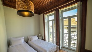 A bedroom with two beds, a wooden ceiling, and a balcony with a metal railing. - Casa com Historia (Covilhã)