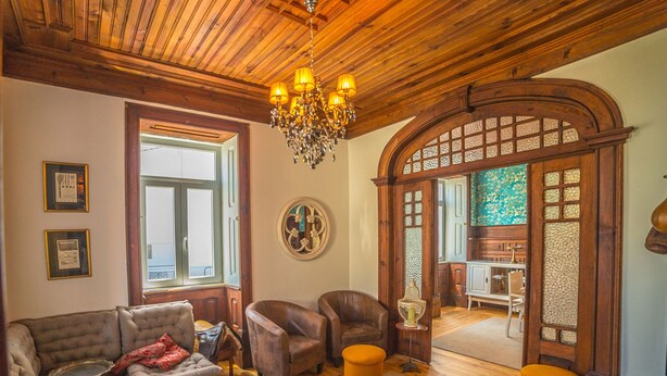A cozy living room with a wooden ceiling, a chandelier, a sofa, armchairs, and a dining area with a wooden cabinet and table. - Casa com Historia (Covilhã)