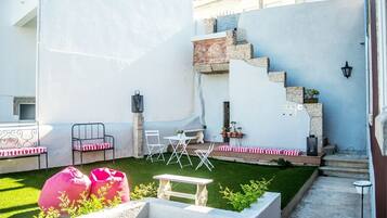 A courtyard with a small lawn, seating area with chairs and a table, a staircase, and a wall with a light fixture.