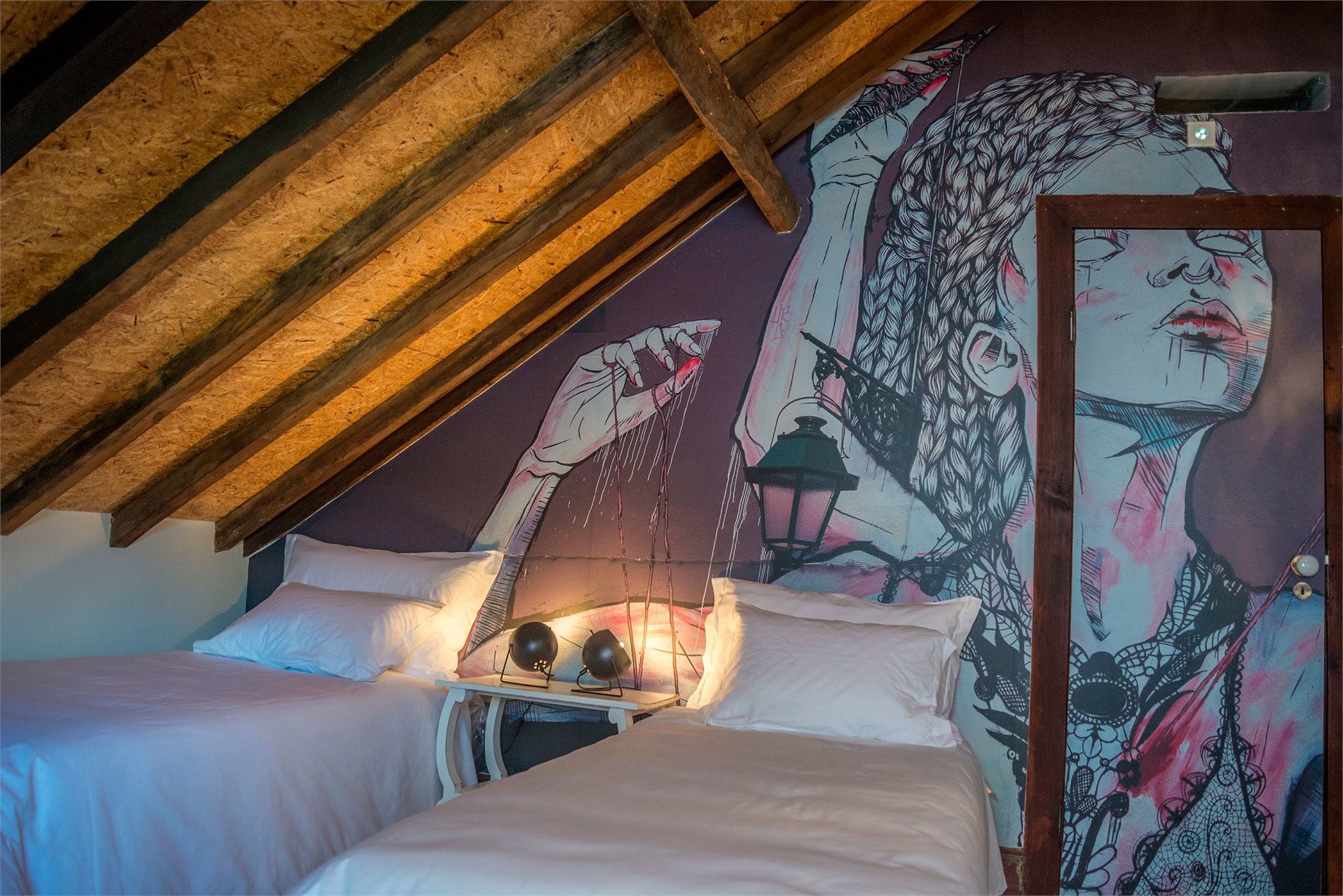 Une chambre avec un plafond en pente, une fresque murale et un lit recouvert de linge de lit blanc.
