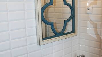 Un baño con paredes de azulejos blancos, un lavabo blanco con un solo grifo y una lámpara de pared.