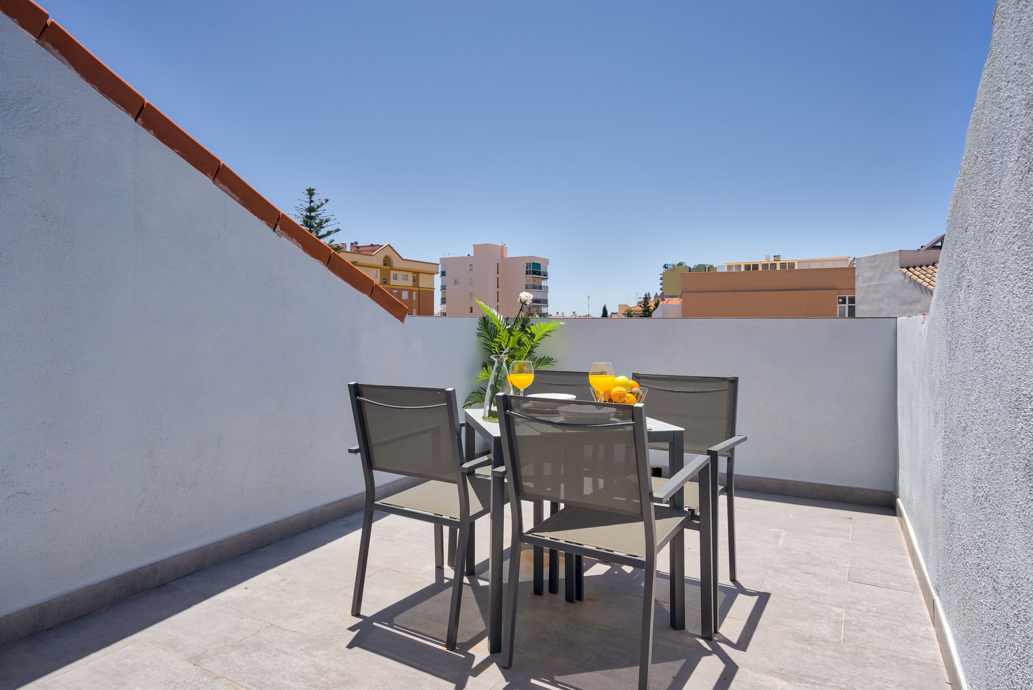 A small outdoor patio with a table and chairs, a potted plant, and a glass of orange juice.
