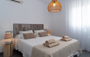 A neatly made bed with a wooden headboard, two bedside lamps, and a large woven light fixture above.