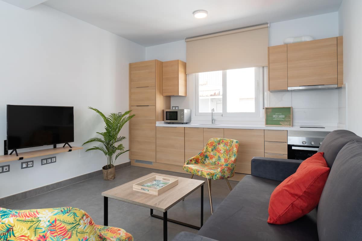 A modern living room with a flat-screen TV, a sofa, a coffee table, and a colorful chair.