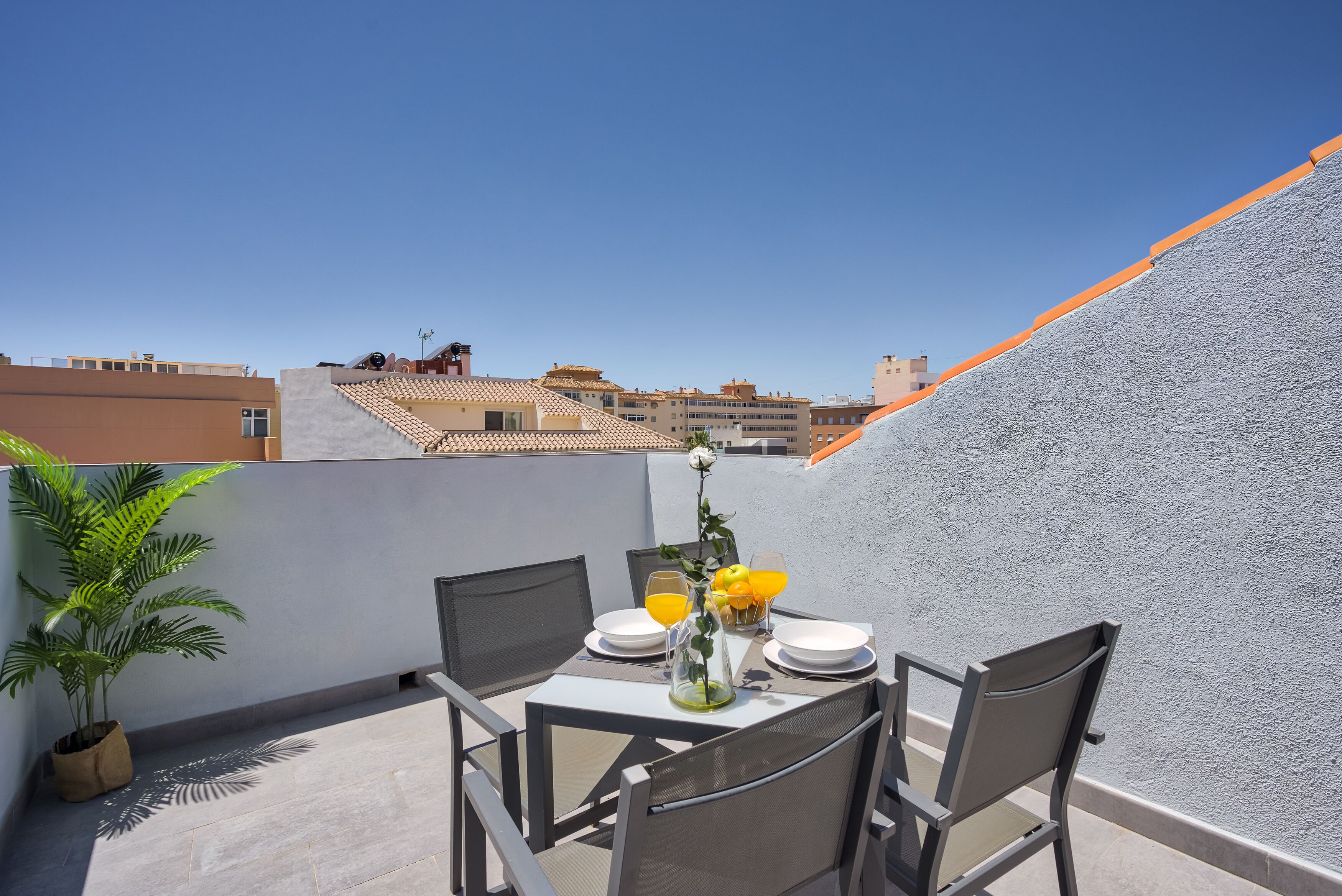 Une terrasse sur le toit avec une table dressée pour deux personnes, agrémentée d’une plante en pot et d’un vase rempli de fleurs.