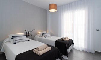 A hotel room with two beds, a hanging light fixture, and sheer curtains.