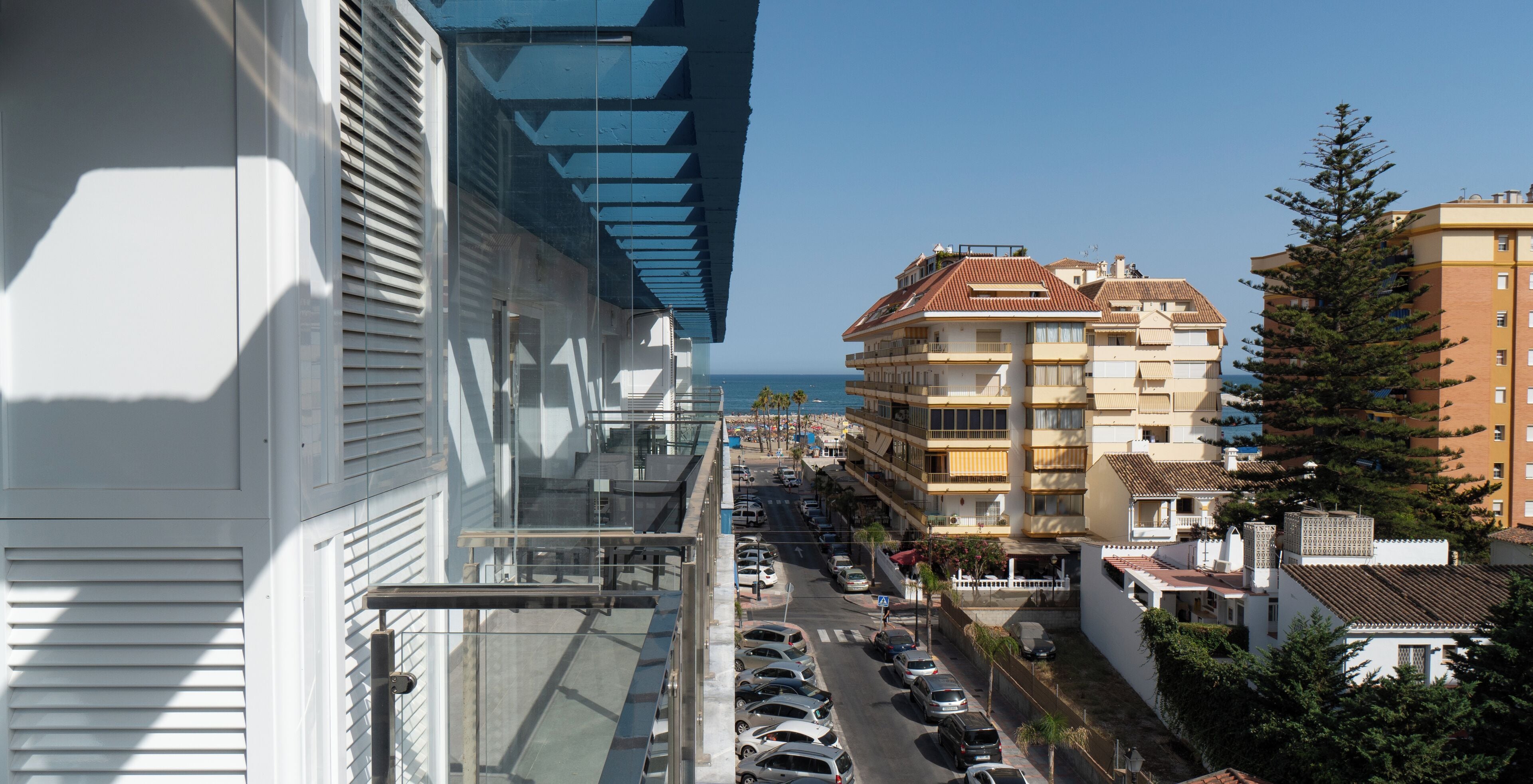 A multi-story building with balconies, a parking lot, and a clear view of the sea.