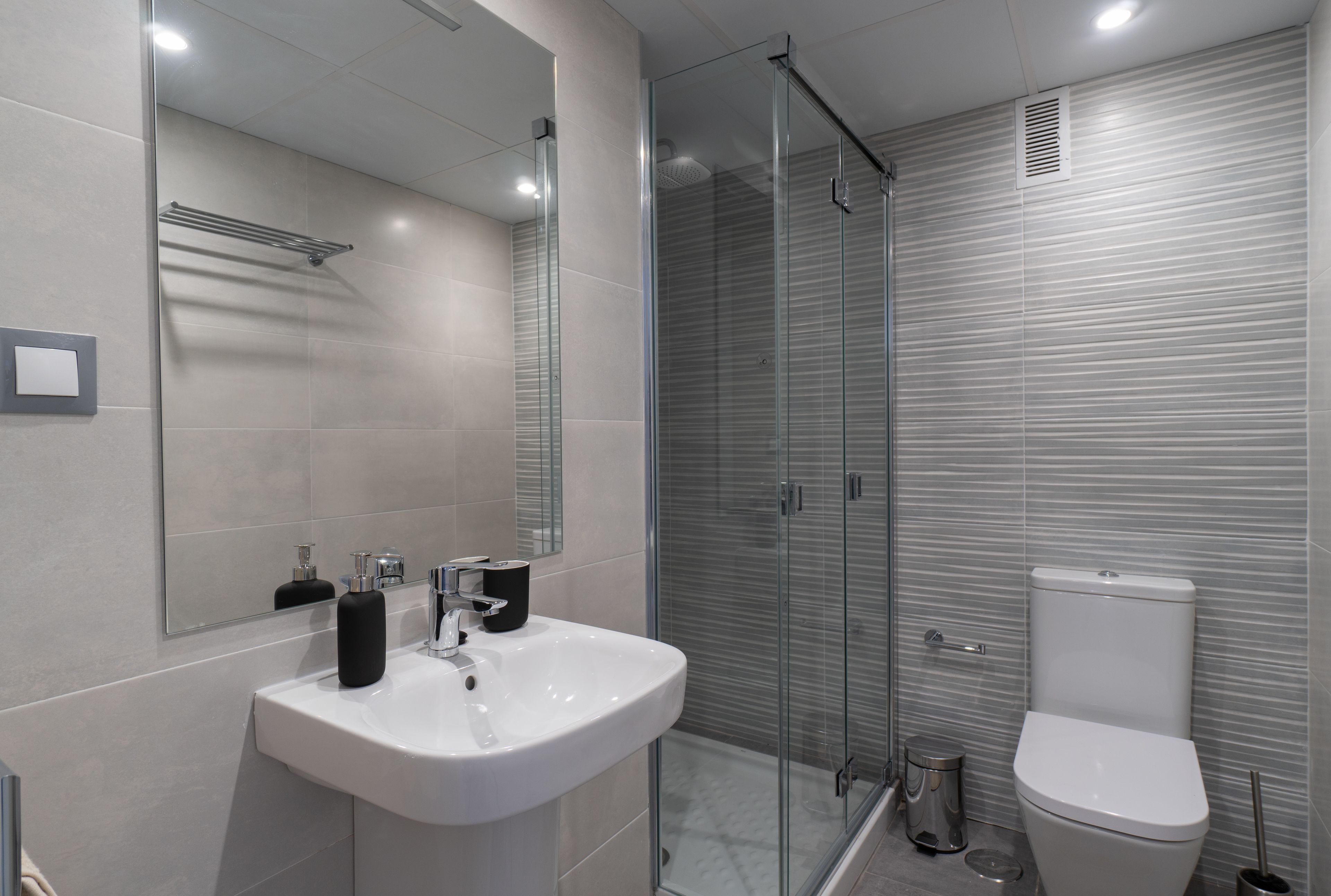 A modern bathroom with a glass-enclosed shower, a white sink, and a toilet.