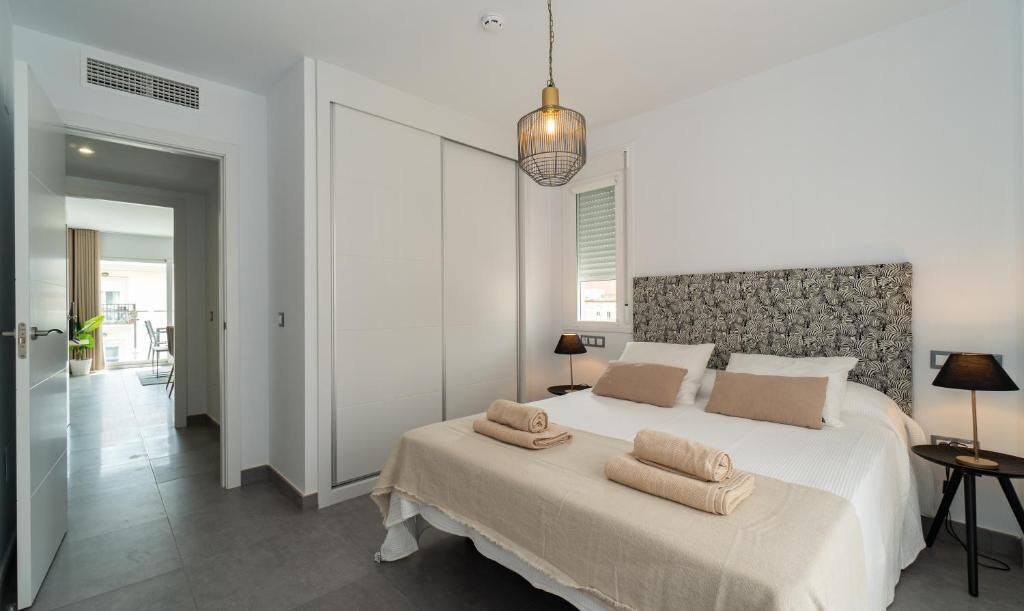 A bedroom with a large bed, two bedside tables, a hanging light fixture, and a view of a balcony.