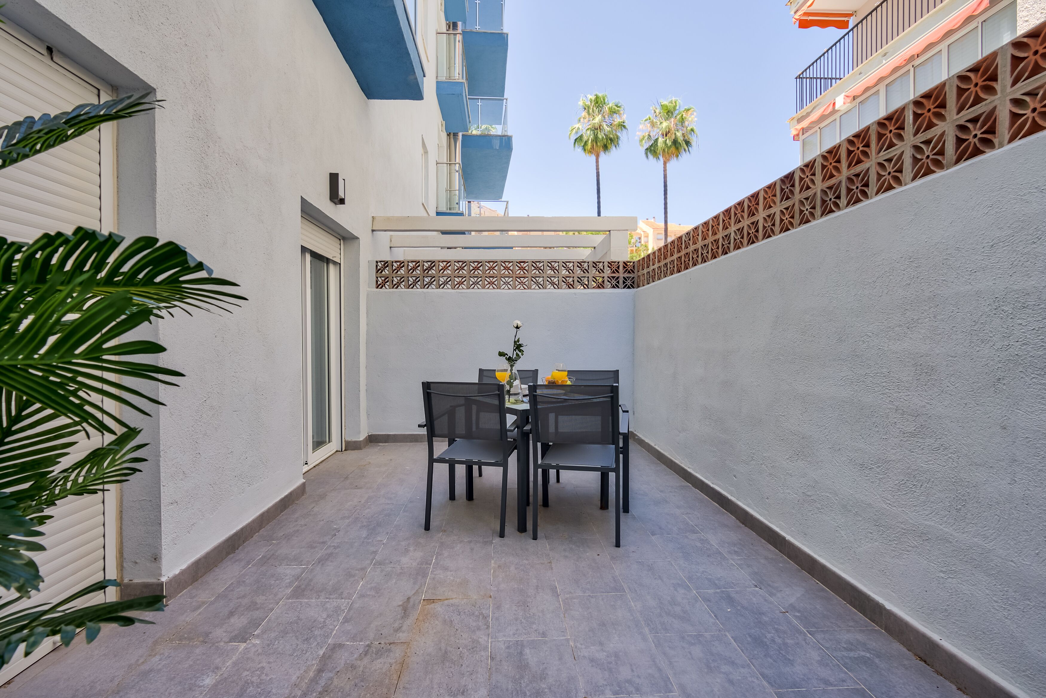 A patio with a table and chairs, a door, and a decorative wall with palm trees in the background.