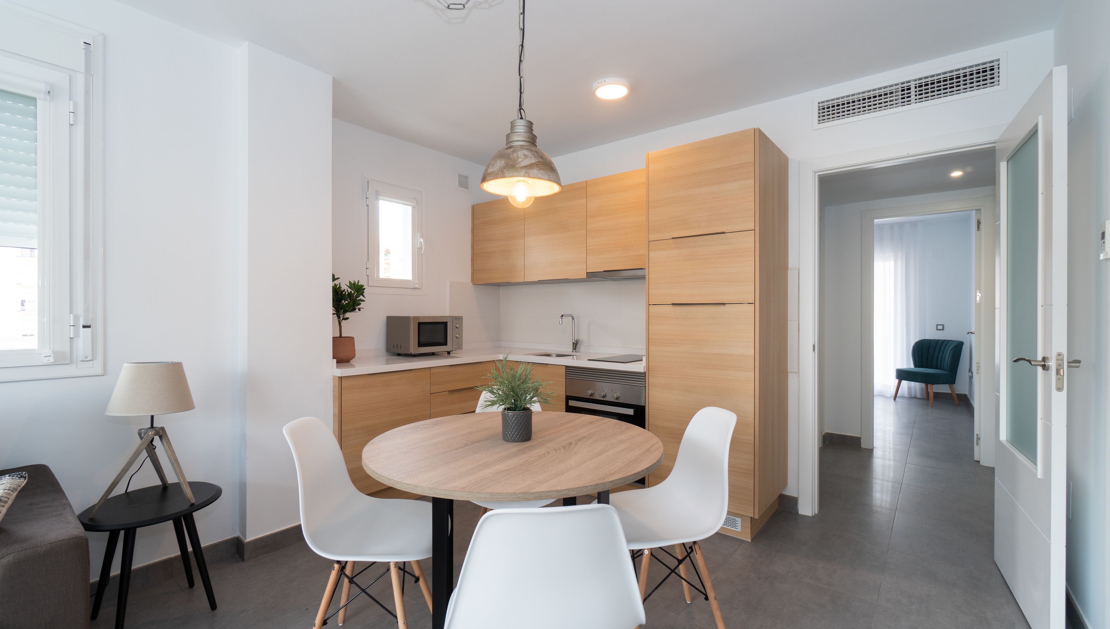 Une cuisine moderne avec des meubles en bois, une table de salle à manger ronde entourée de chaises blanches, un four à micro-ondes et une plante en pot.