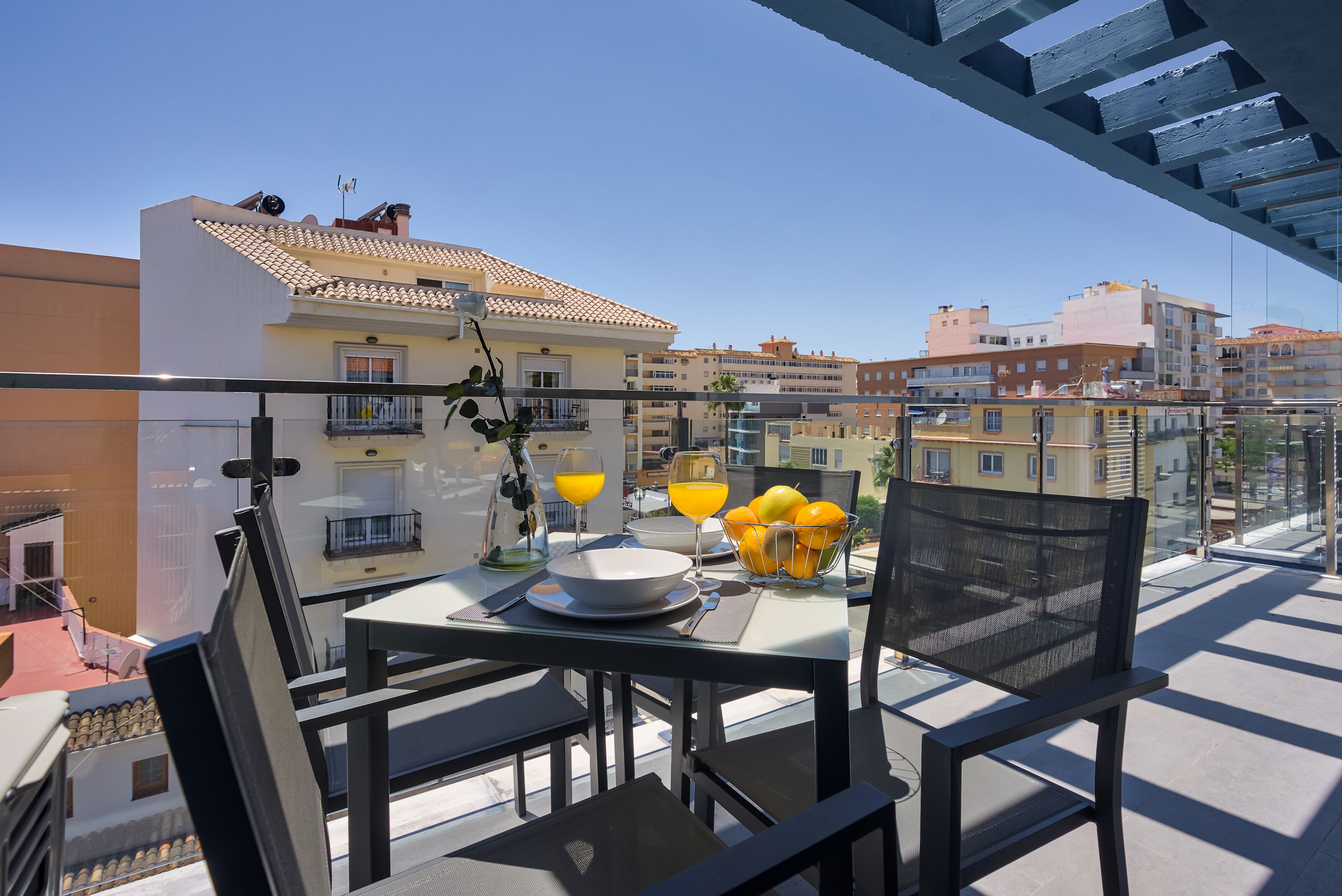 Un balcone con un tavolo apparecchiato per la colazione, con succo d'arancia e una ciotola di frutta.