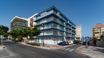 A multi-story hotel with balconies, a pedestrian crossing, and parked cars on the street.
