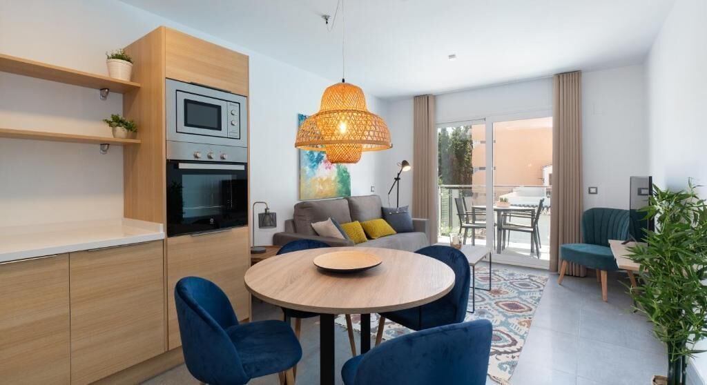 Una cocina moderna con electrodomésticos integrados, un comedor con sillas azules y un amplio ventanal con vistas a un balcón.