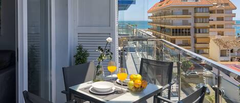 A balcony with a table set for breakfast, including plates, glasses, and a fruit bowl.
