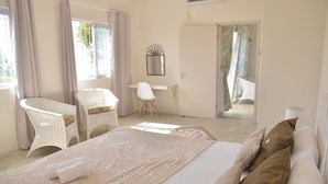 A bedroom with a large bed, two white wicker chairs, a small desk, and a view of the outside balcony. - Villa Zourit Rodrigues Bungalow (Rodrigues Island)