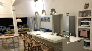 A modern kitchen with a central island, bar stools, pendant lighting, and a dining area with a table and chairs. - Villa Zourit Rodrigues Bungalow (Rodrigues Island)