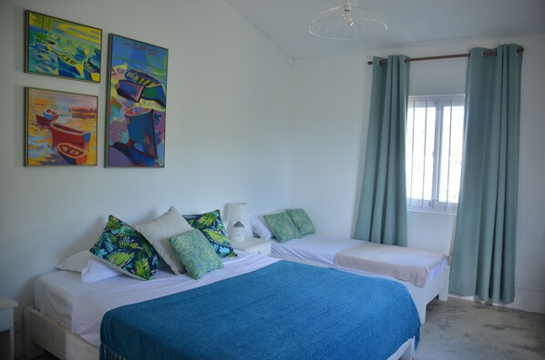 A bedroom with two beds, a window with curtains, and three paintings on the wall.