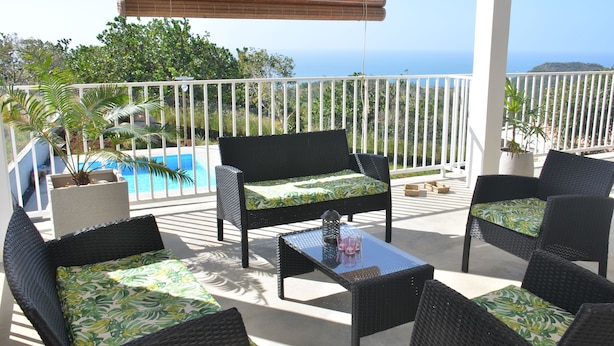 A balcony with wicker furniture, a glass table, and a view of the ocean. - Villa Zourit Rodrigues Bungalow (Rodrigues Island)