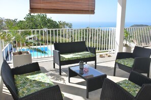 A balcony with wicker furniture, a glass table, and a view of the ocean.