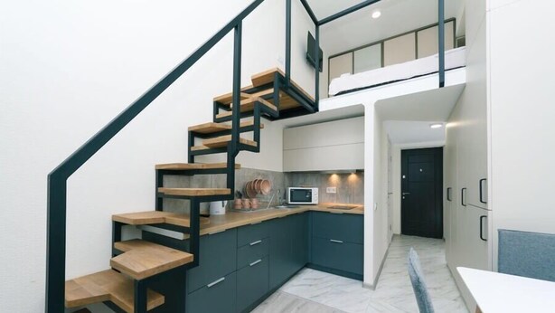 A modern kitchen with dark cabinets, a wooden staircase, and a small dining area.