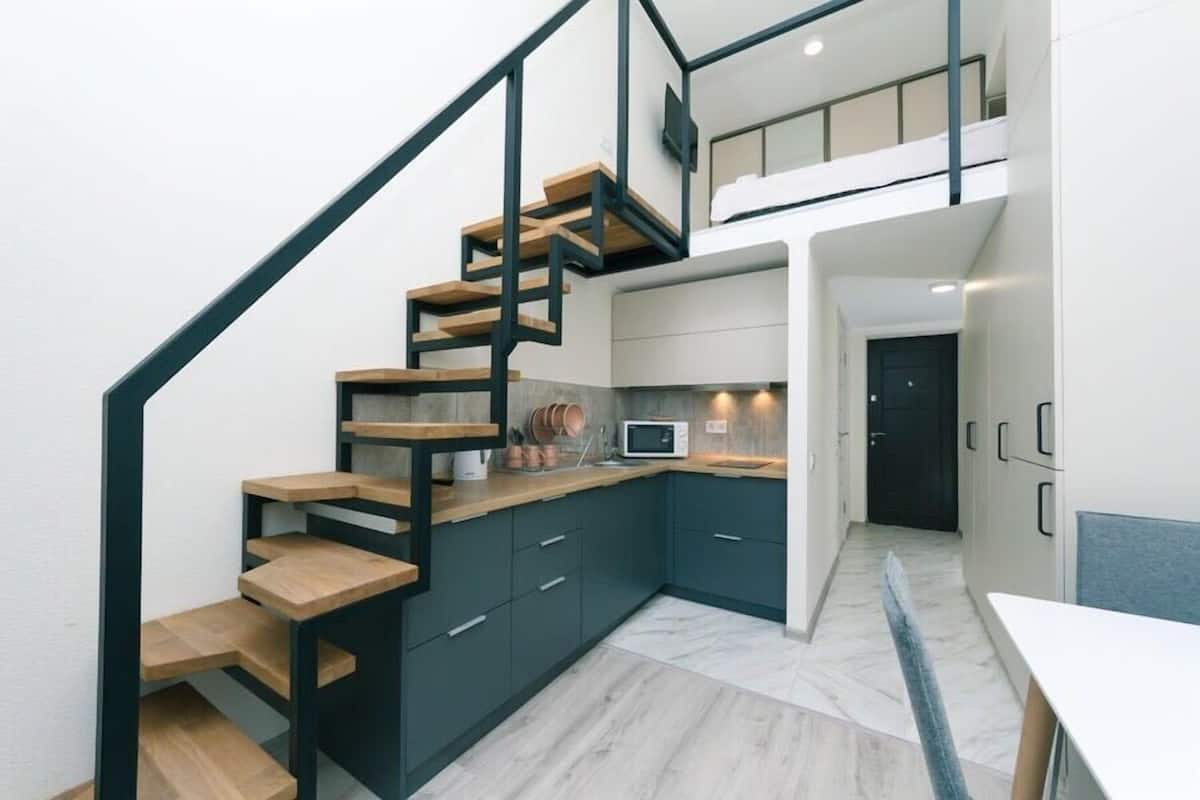 A modern kitchen with dark cabinets, a wooden staircase, and a small dining area.
