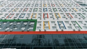 A modern building with a grid of windows and air conditioning units, featuring a red, green, and yellow stripe pattern.