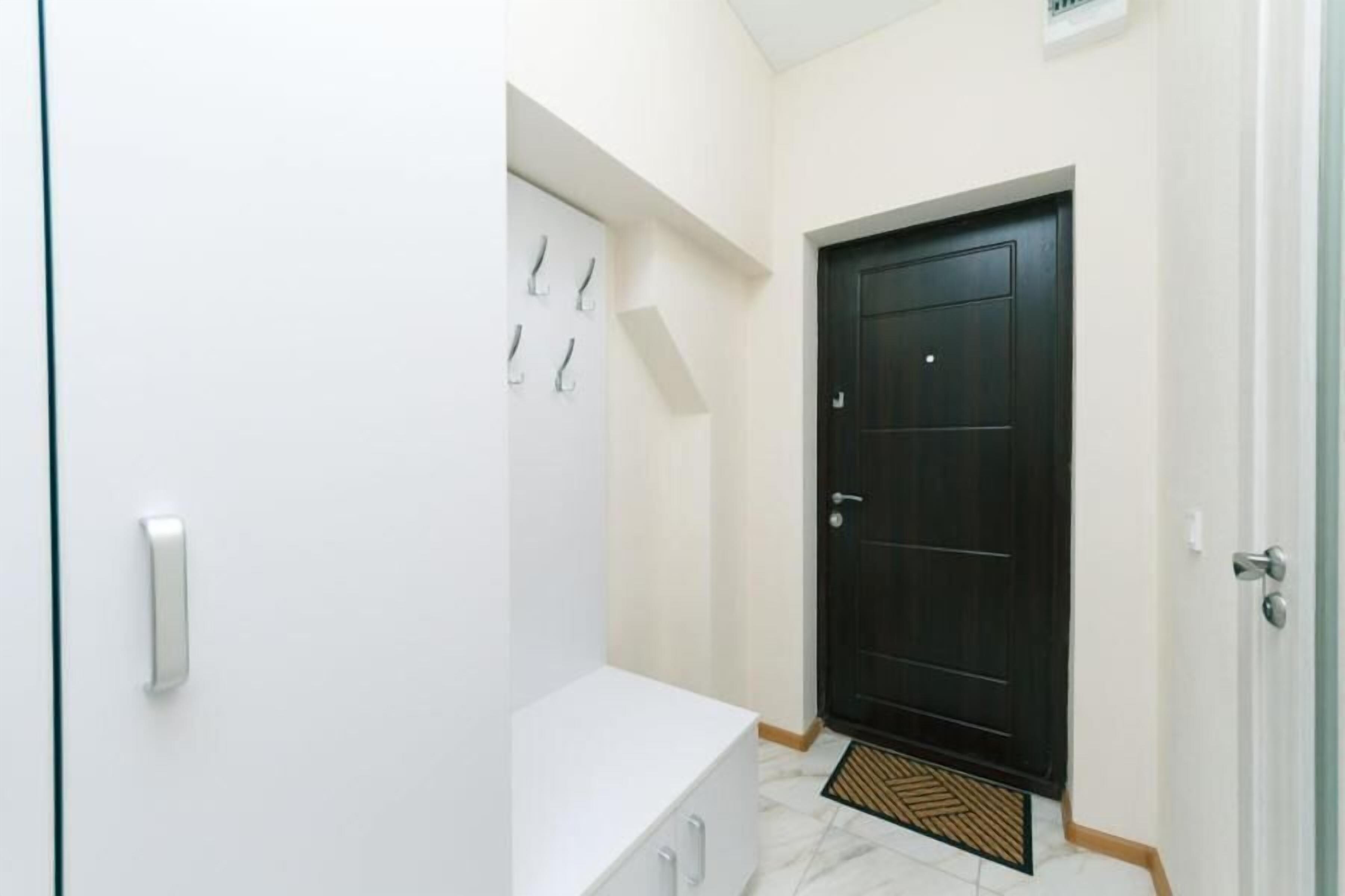A hallway with a white wall, a black door, and a white bench.