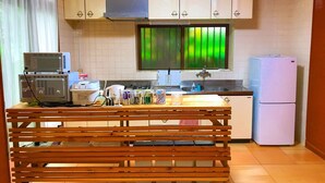 Una cocina con armarios blancos, un microondas, un refrigerador y una ventana con vista a árboles verdes.